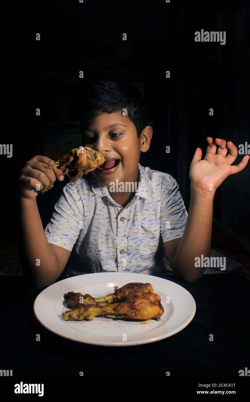 Indiano Kid mangiare pollo fritto drumstick. Bambino che ha un briciola di pollo da mangiare. Bambino con arrosto di pollo yummy. Foto Stock