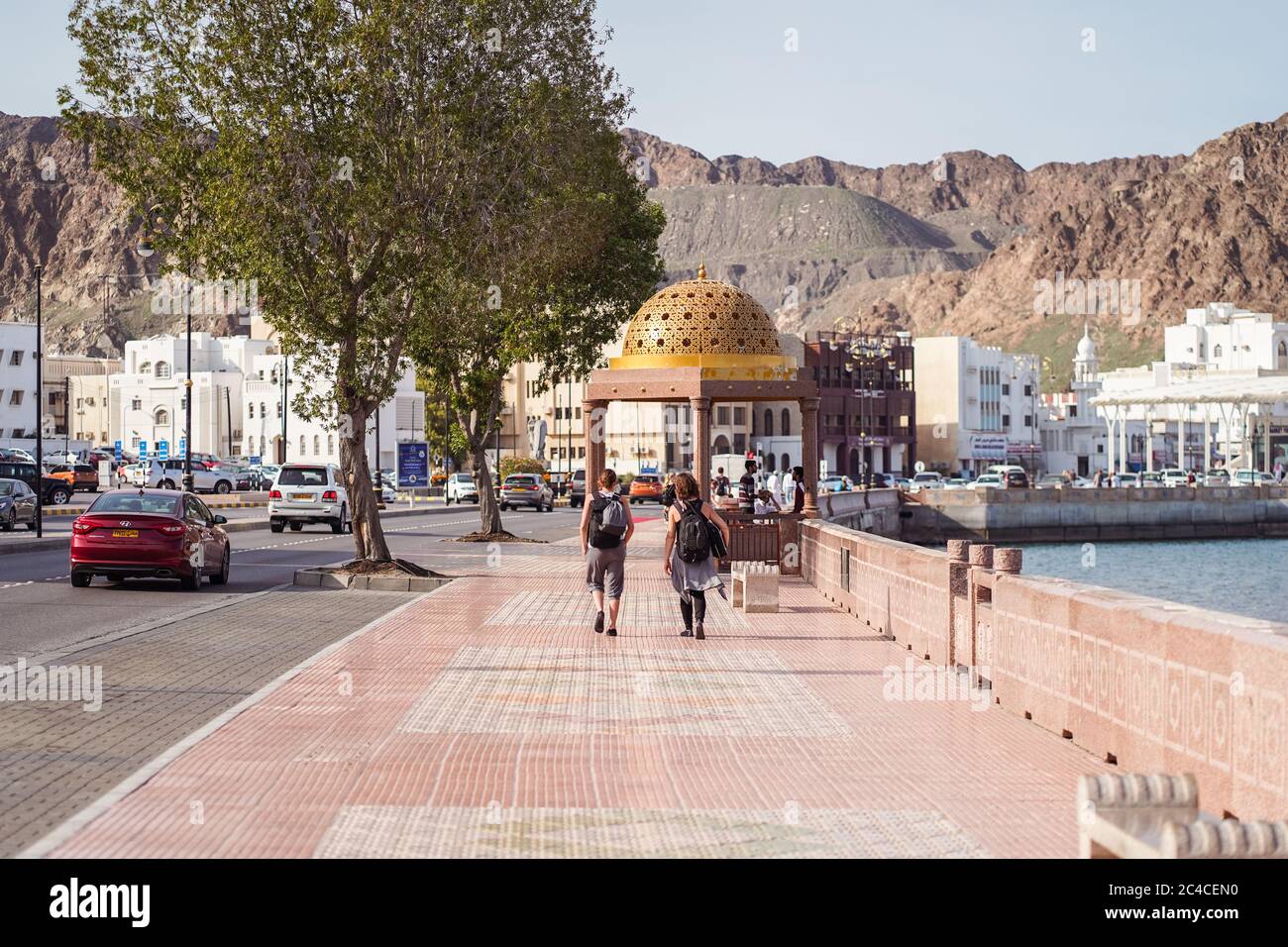 Mascate / Oman - 15 febbraio 2020: Turisti occidentali nella Corniche di Mascate con vista sull'acqua e grande nave da crociera turistica nel porto Foto Stock