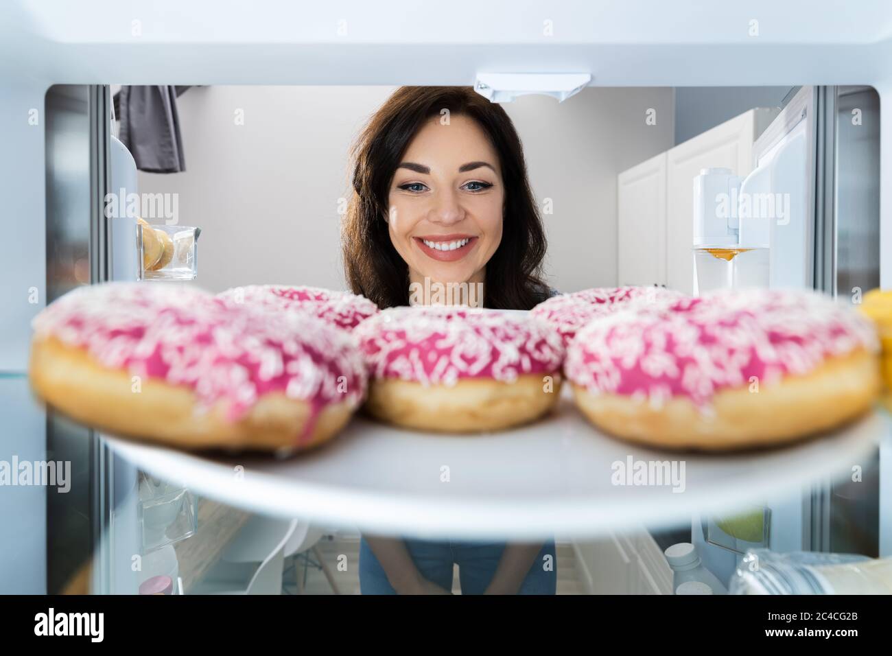 Happy Young Woman guardando Donut da frigorifero o congelatore Foto Stock