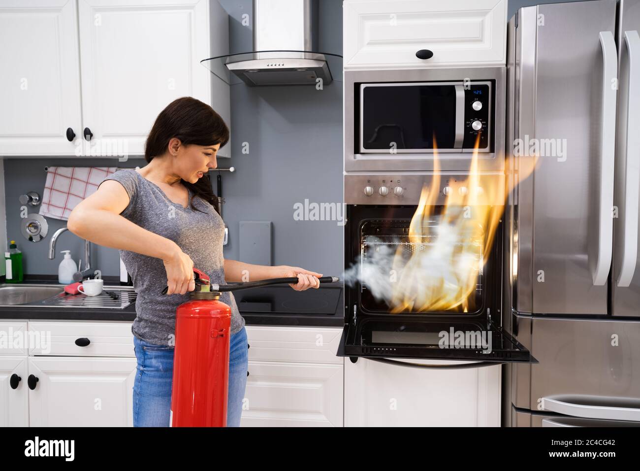 Giovane donna con un estintore per spegnere un incendio dal forno a casa Foto Stock
