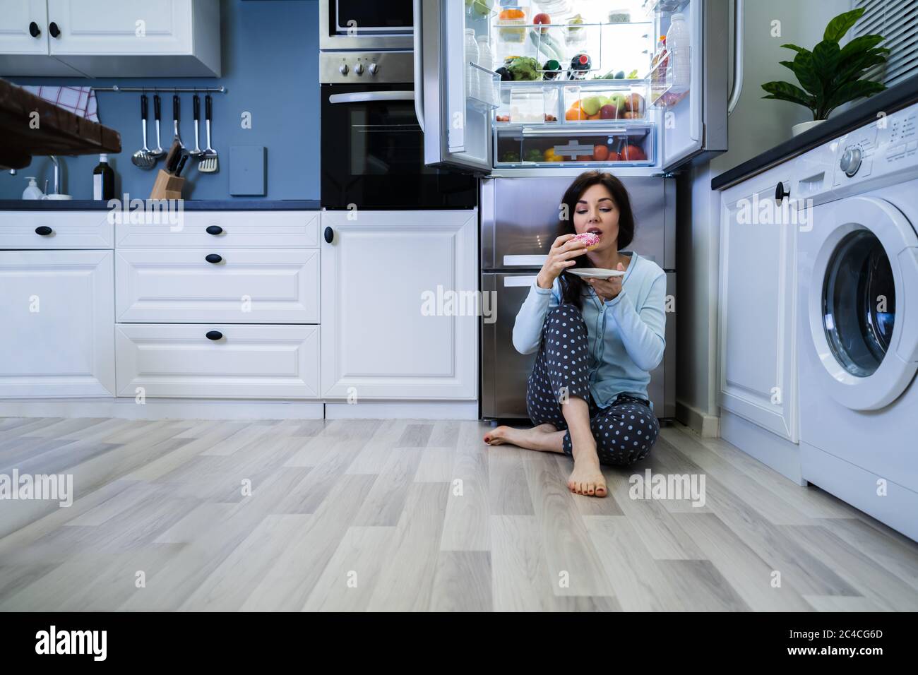 Indulgenza dolce di notte aperta. Donna che mangia vicino al frigorifero Foto Stock