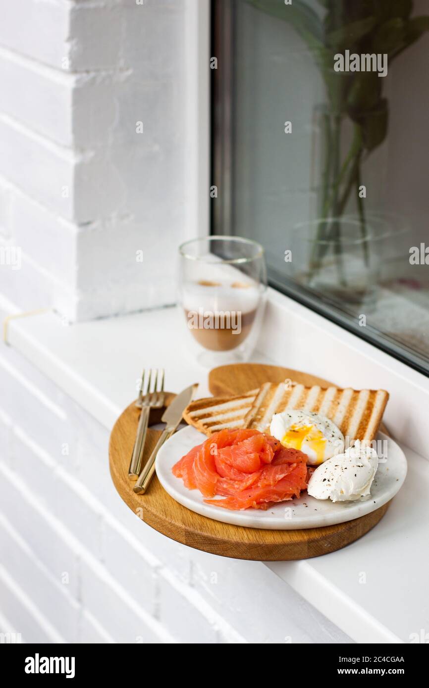 Menu colazione: Pane tostato, salmone affumicato, uova in camicia e tazza di caffè sul davanzale bianco Foto Stock