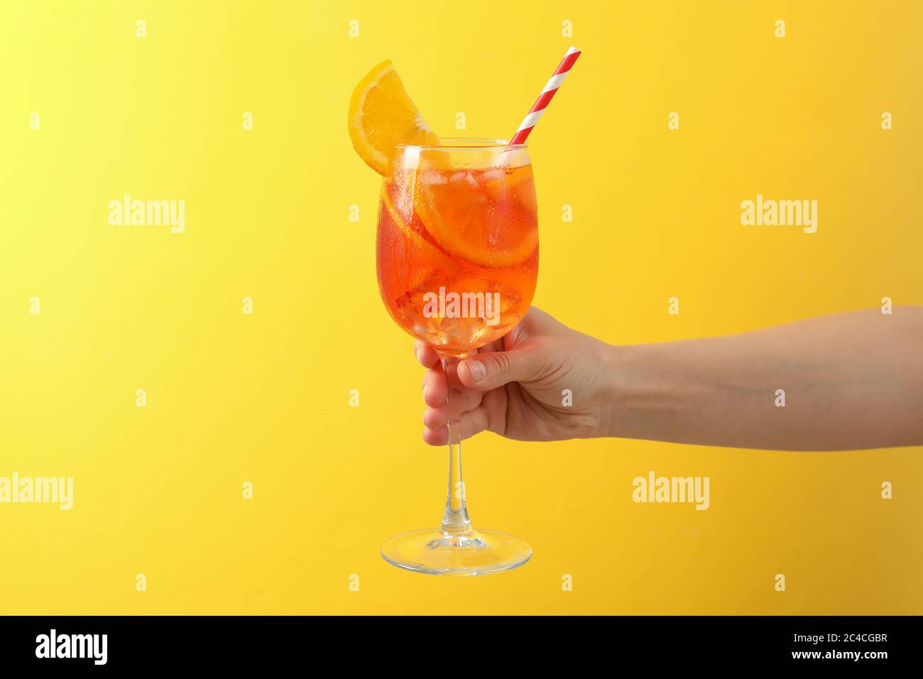 Mano femminile con bicchiere di aperol Spritz cocktail su sfondo giallo Foto Stock