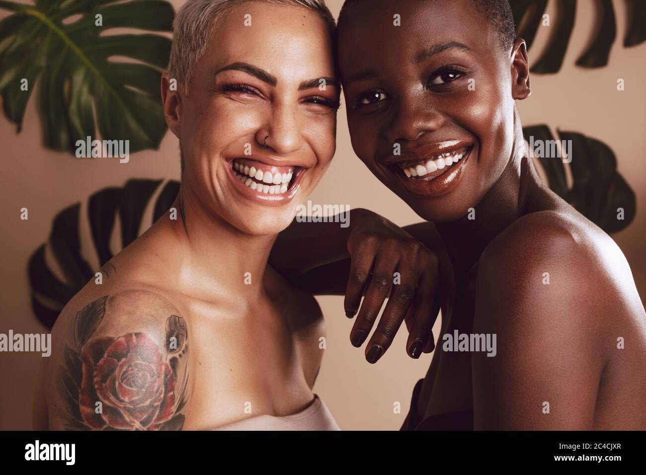 Felice modelli femminili guardando la macchina fotografica contro foglie in background. Due donne multietniche che si levano in piedi insieme e sorridono. Foto Stock