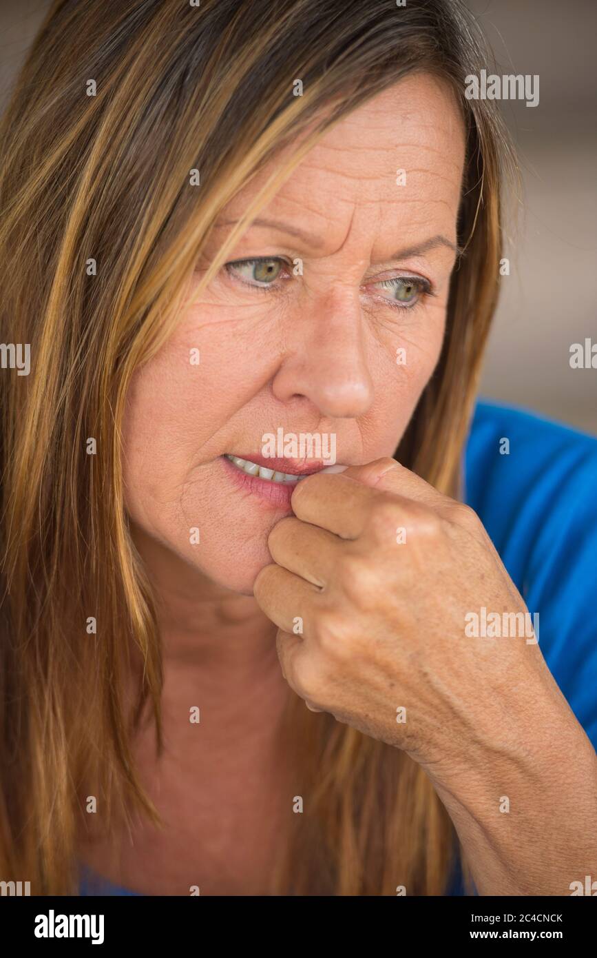 Ritratto attraente donna matura con nervosa insicura espressione del viso stressata, mordere unghie dita, sfondo sfocato. Foto Stock