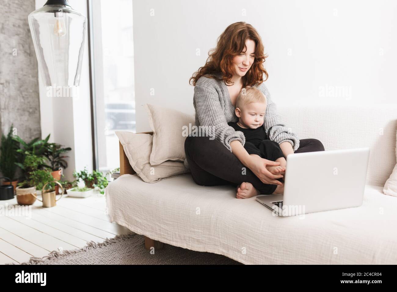 Giovane bella donna seduta sul divano con il suo piccolo bel figlio sognando usando il laptop insieme. Mamma con bambino ragazzo felice di trascorrere il tempo in vita Foto Stock