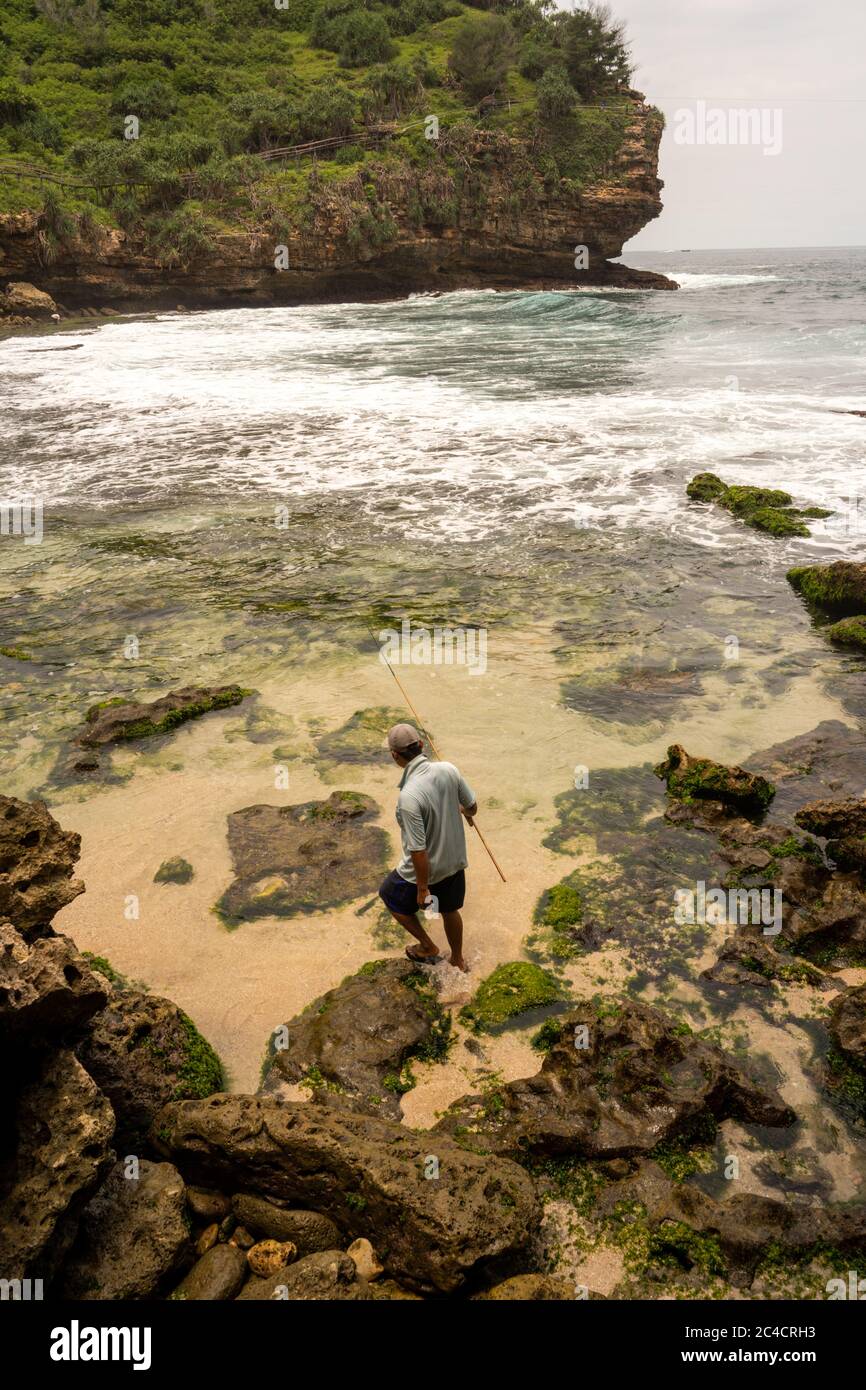 Un pescatore indonesiano solista cammina lungo una costa rocciosa. Foto Stock