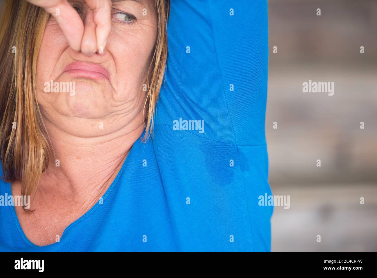 Ritratto donna matura con sudore sudore puzzolente sotto il braccio con punto di umidità bagnato sulla camicia, sfondo sfocato, spazio copia. Foto Stock