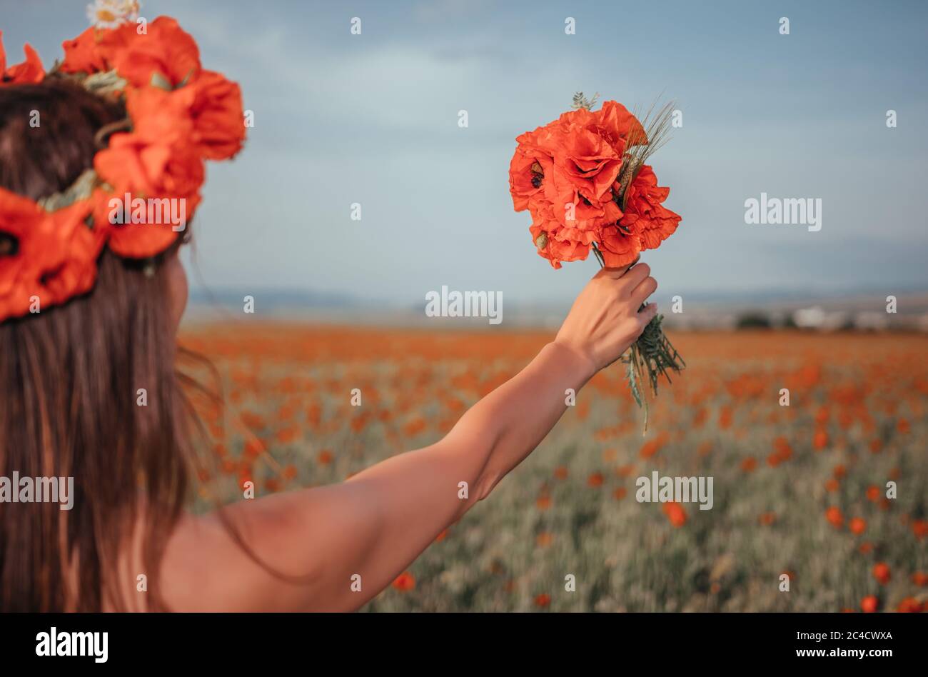 Sposa in un abito bianco che tiene un bouquet di fiori di papavero, caldo tempo di tramonto sullo sfondo del campo di papavero rosso. Spazio di copia. Il concetto di Foto Stock