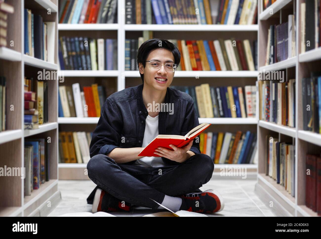 Sorridente ragazzo cinese che legge libri alla biblioteca Foto Stock