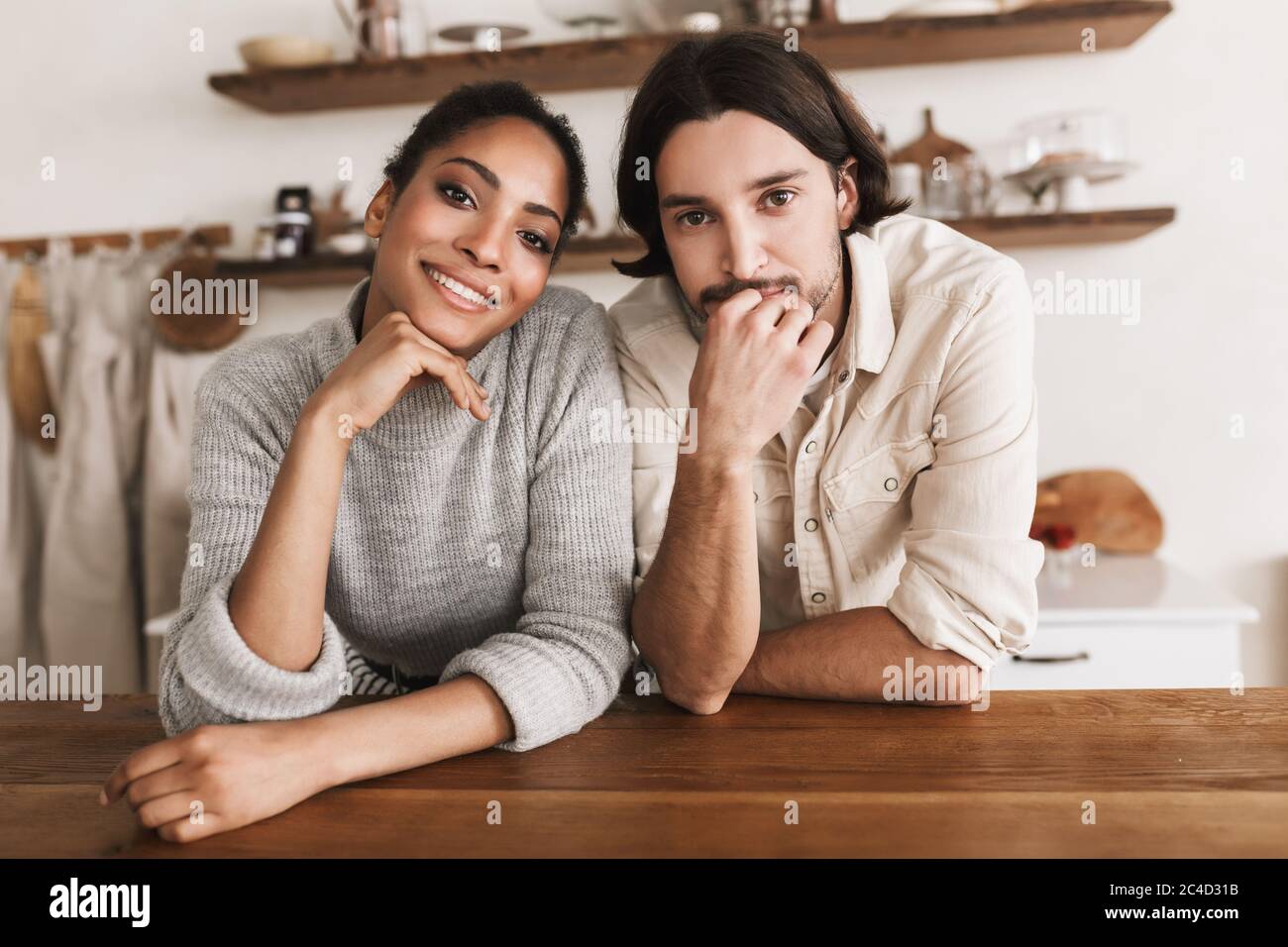 Uomo attraente e bella donna afroamericana sorridente appoggiata sul tavolo che guarda felicemente in macchina fotografica insieme. Giovane coppia internazionale sognata Foto Stock