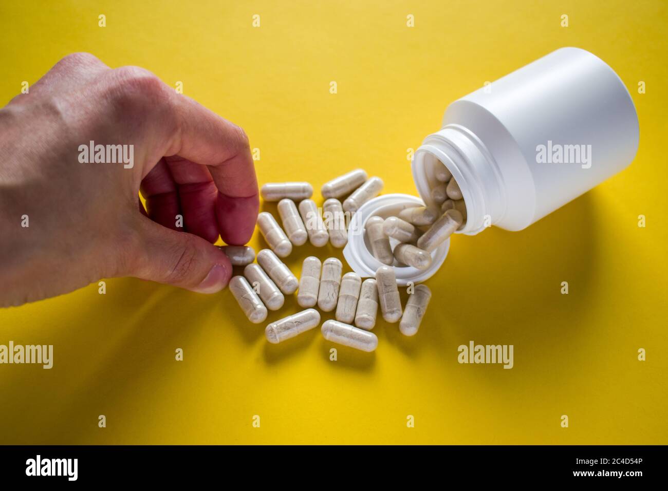 Mano prendendo spilled pillole mediche dal flacone di pillola su sfondo giallo Foto Stock