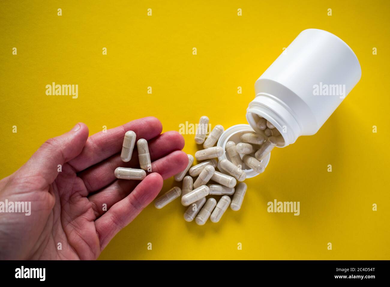 Mano che tiene versato pillole mediche dal flacone pillola su sfondo giallo Foto Stock