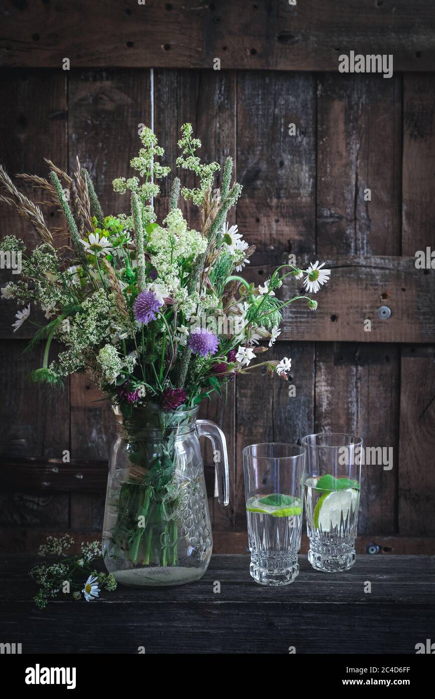 Paesaggio di campagna con fiori selvatici in vaso e bicchieri con acqua Foto Stock