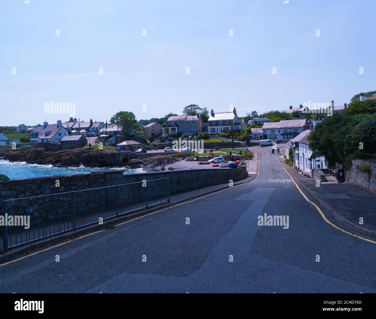 Vista lungo la strada principale di questo piccolo villaggio di pescatori Moelfre Isola di Anglesey Galles del Nord UK con barche a remi tirate su una spiaggia di ciottoli su una bella somma Foto Stock
