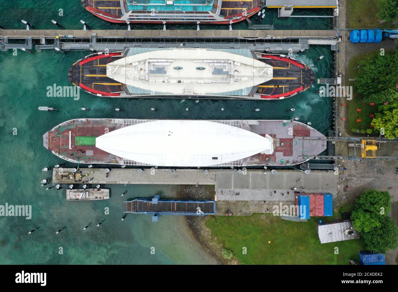 Konstanz, Germania. 26 Giugno 2020. Il guscio di un nuovo traghetto (sotto) viene attratto nel porto dei traghetti dopo che è stato spinto attraverso il lago di Costanza da un altro traghetto (sparato con il drone). Per la prima volta, il traghetto ha un nuovo strato di vernice. Invece di blu e bianco come i vecchi traghetti, il nuovo traghetto è ora rosso-bianco. Credit: Felix Kästle/dpa/Alamy Live News Foto Stock