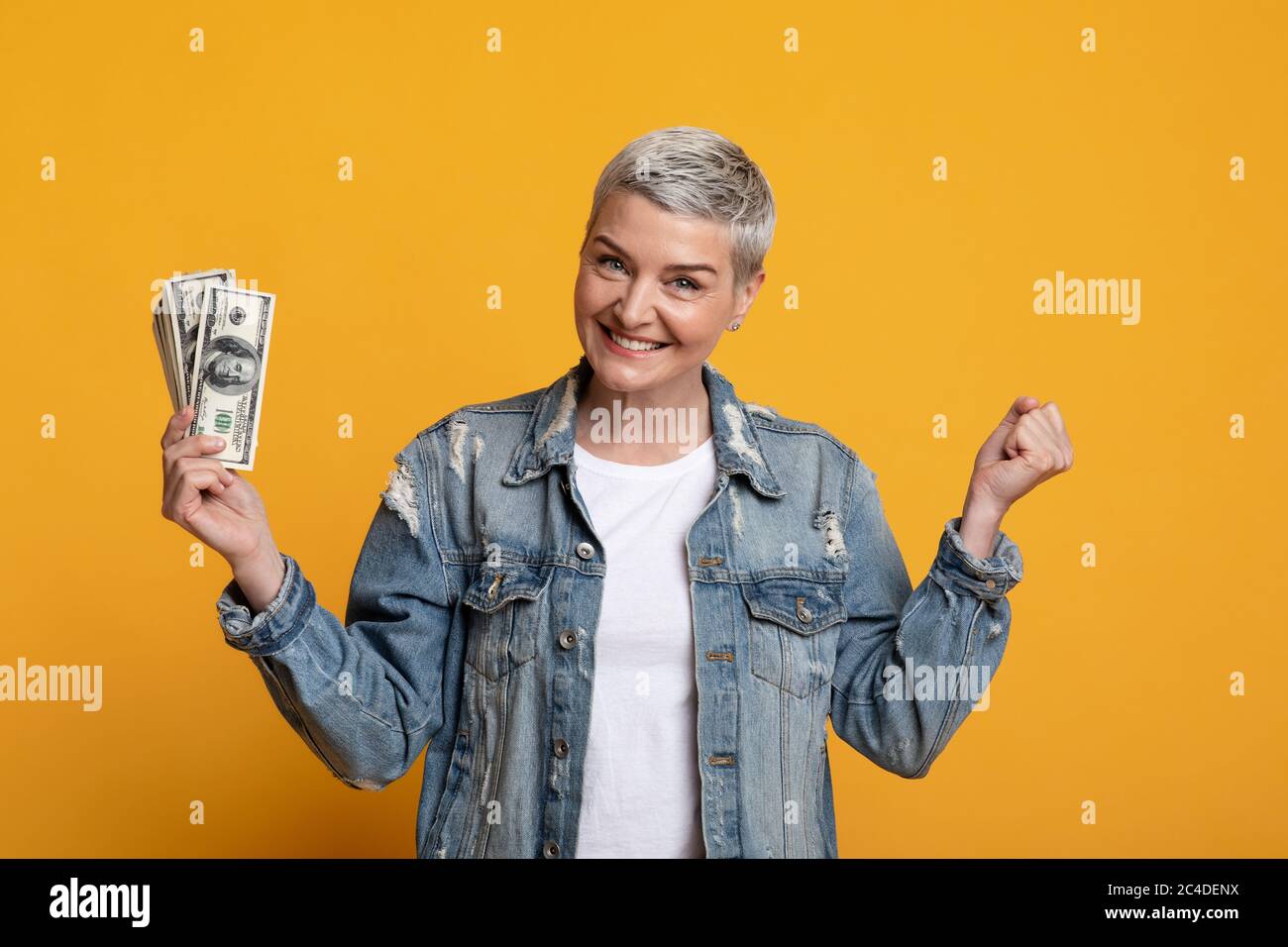 Grande fortuna. Eccitato Donna matura che tiene Dollar Cash, gesturing Sì, celebrando il successo Foto Stock