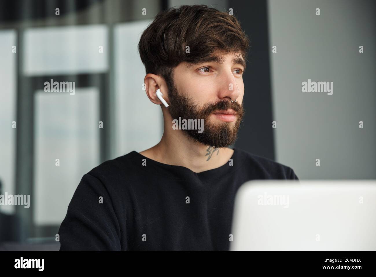 Immagine di un giovane uomo serio che utilizza auricolari wireless e lavora con un computer portatile in salotto Foto Stock