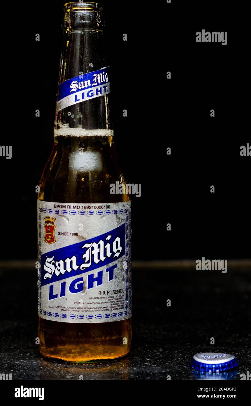 Vista frontale della birra San Miguel Light con etichetta argentata e blu e coperchio accanto a essa su sfondo in marmo nero Foto Stock