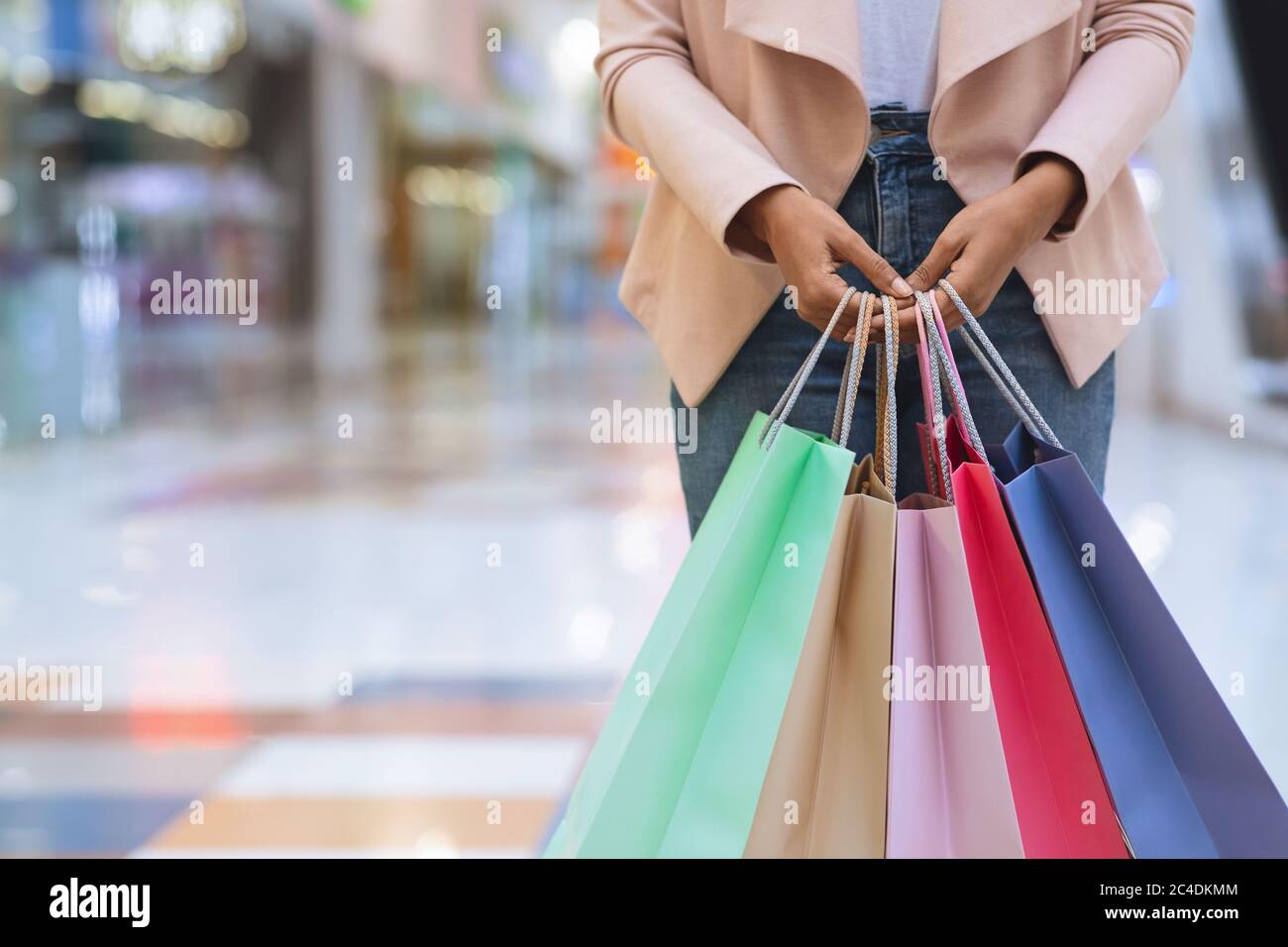 Donna nera irriconoscibile in piedi con un sacco di borse colorate per lo shopping nel centro commerciale Foto Stock