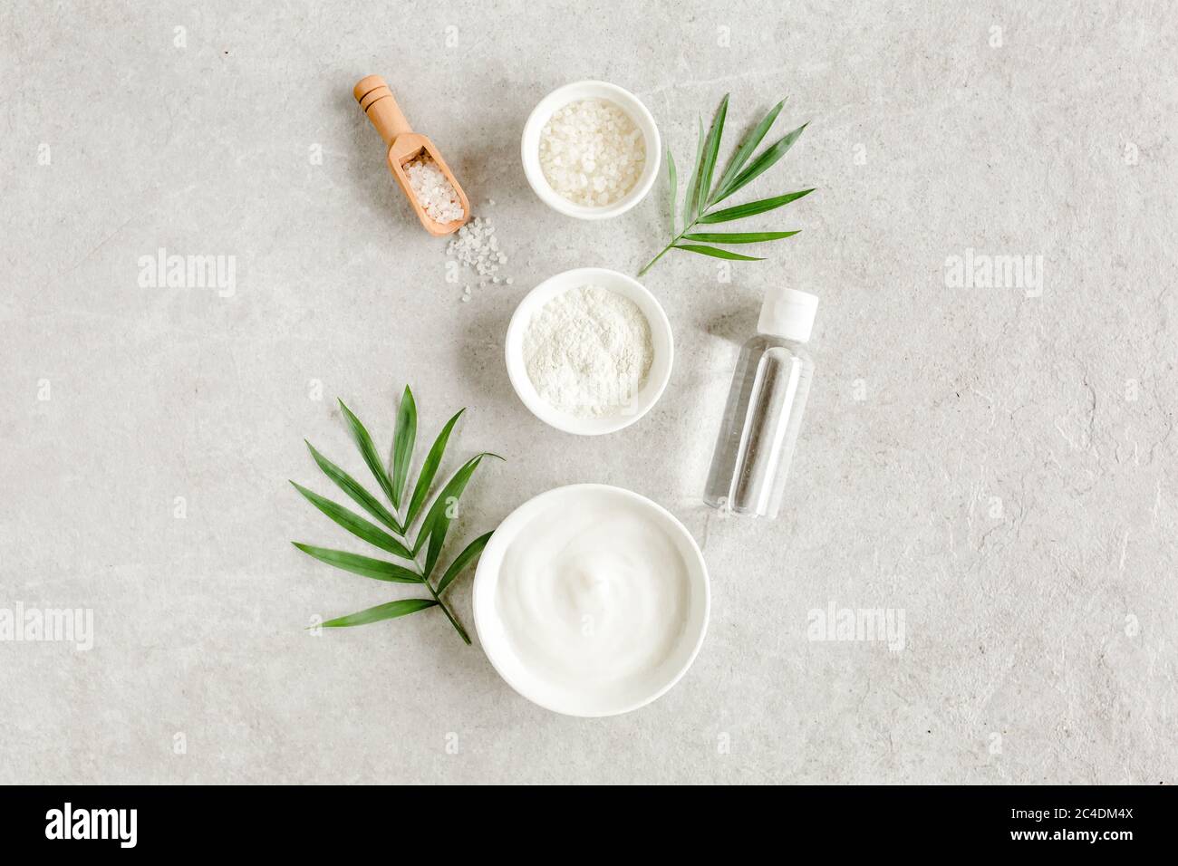 Set prodotti cosmetici per la cura della pelle e del corpo femminile: Crema viso, argilla cosmetica, sale marino, bottiglia con ialuronico su sfondo grigio marmo. Foto Stock