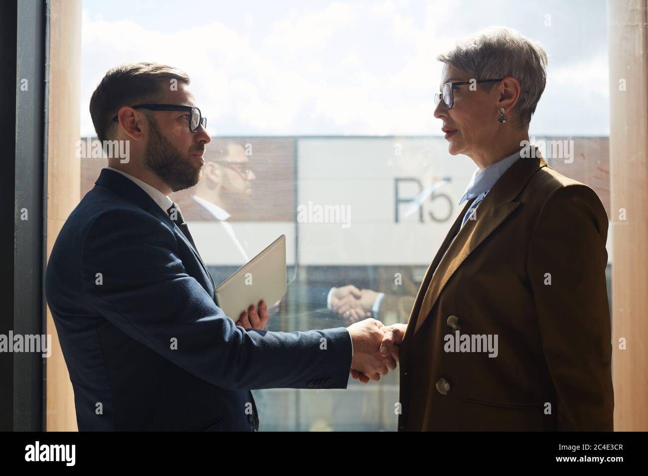 I partner aziendali si contrappone alla grande finestra dell'ufficio e scuotono le mani Foto Stock