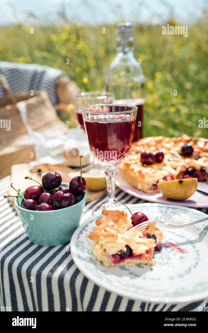 Tavolo in giardino servito con bei bicchieri da vino d'annata, piatti, posate e stoviglie d'argento, tovaglie, torta di ciliegie dolci e ciliegie fresche stil Foto Stock