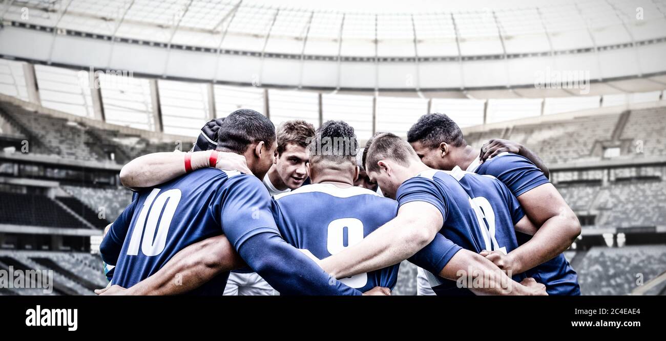 Immagine digitale composita di una squadra di giocatori di rugby in piedi in un huddle in uno stadio sportivo Foto Stock