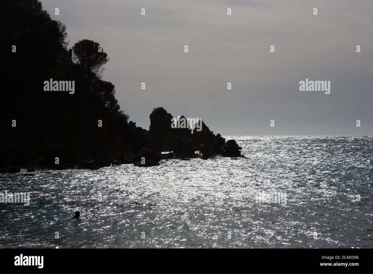 Spiaggia in controluce a Paleaokastritsa con sagome di scogliere e alberi Foto Stock