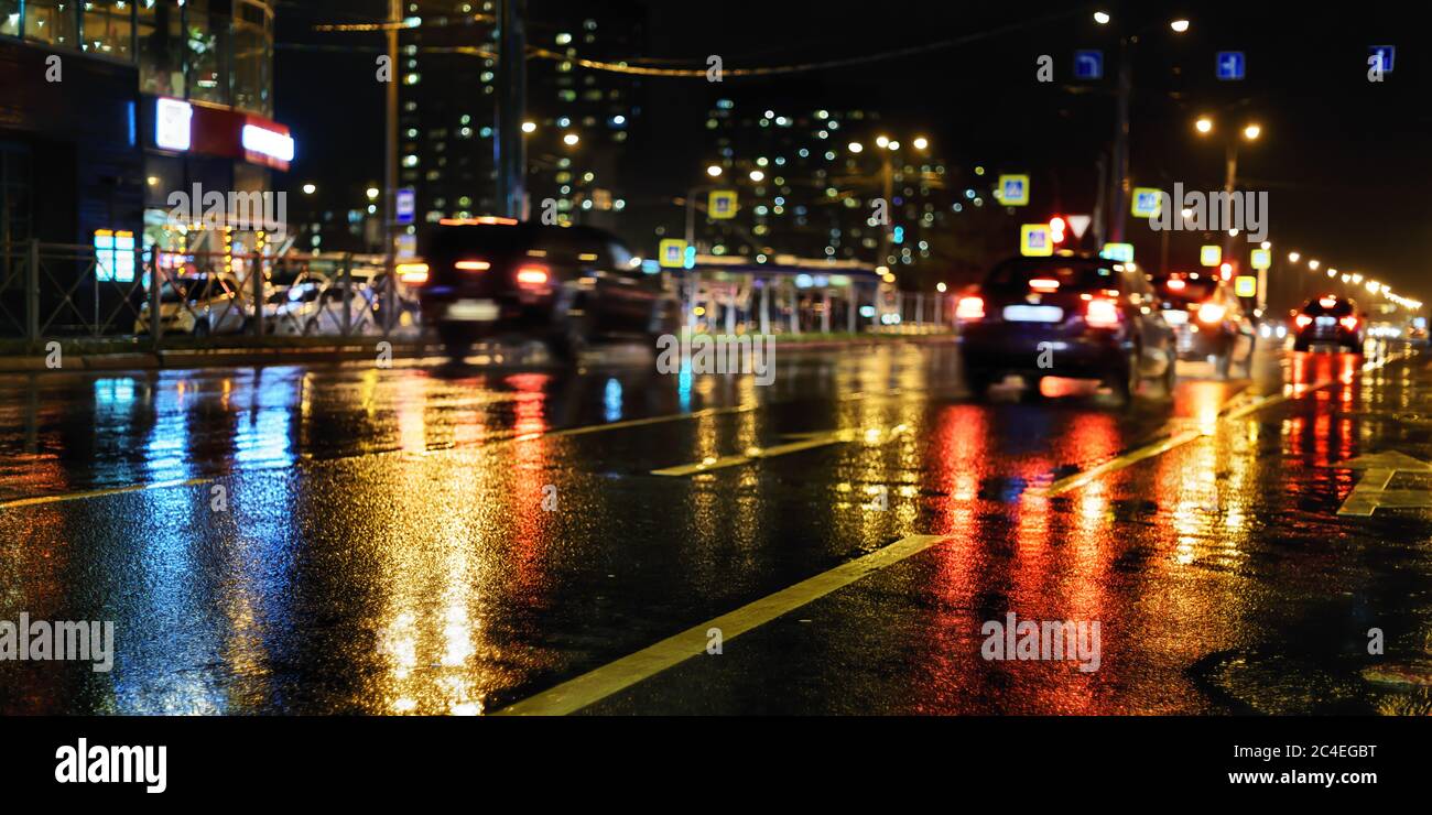 Notte piovosa in città. Strada bagnata, auto, riflessi di luci colorate e silhouette sfocate Foto Stock