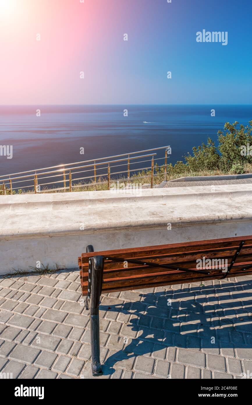 Panca vuota sulla riva del mare in un parco. Vista mare dalla montagna. Concetto di viaggio, relax o solitudine. Panca di legno su spazio aperto che si affaccia su una bella Foto Stock