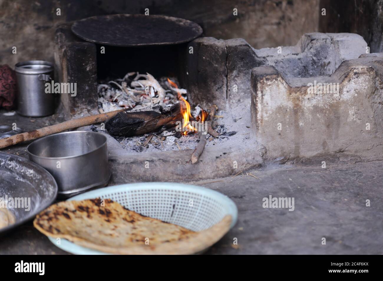 Cucinare un pasto su una stufa di villaggio usando legno per il fuoco. Pane piatto visto in primo piano Foto Stock