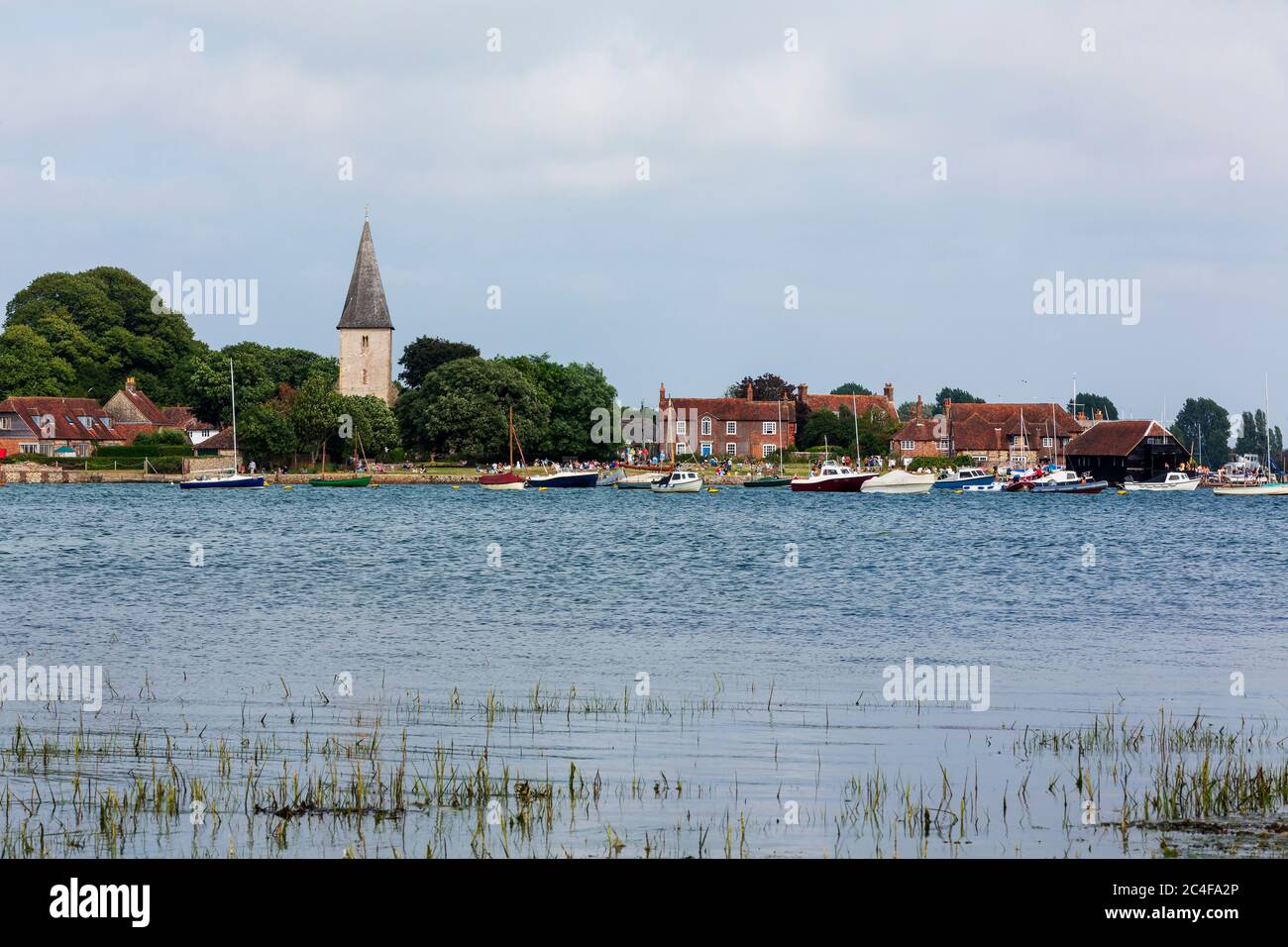 Alta marea Bosham nel Sussex occidentale attraverso il porto di Chichester in un giorno estivo. Villeggianti e picnic sul prato di fronte alla Santissima Trinità. Foto Stock