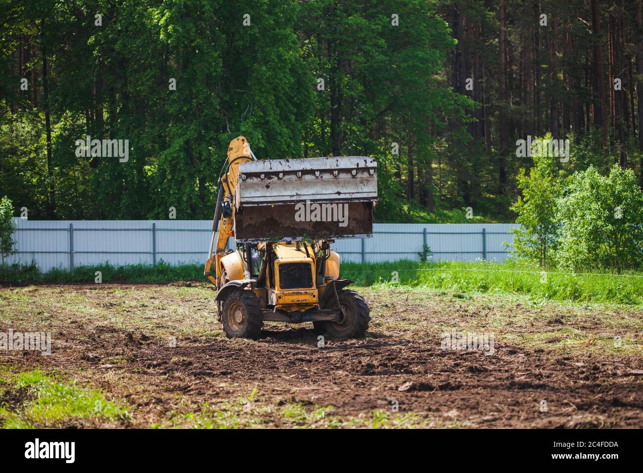Compensazione e livellamento di un terreno privato. Escavatore giallo con benna grande e aperta Foto Stock