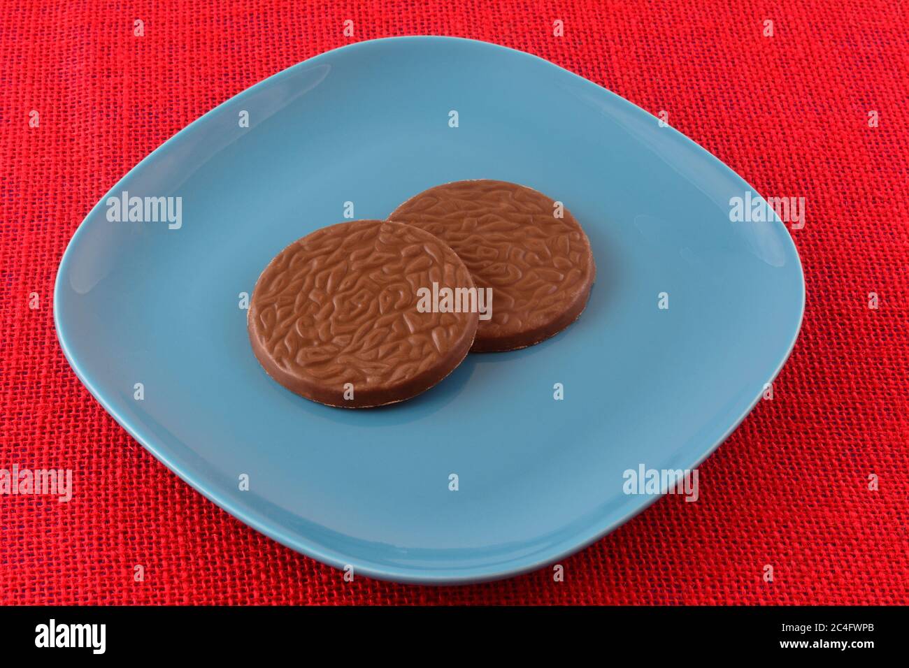 Caramella al cocco al cioccolato su piatto da dessert blu su tovaglia rossa Foto Stock