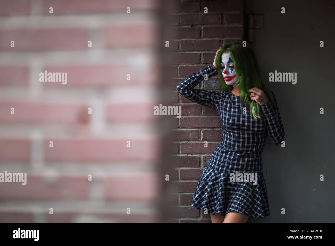 Ritratto di una ragazza con capelli verdi in abito da masticare con trucco joker su una parete di mattoni sfondo sfocato. Foto Stock