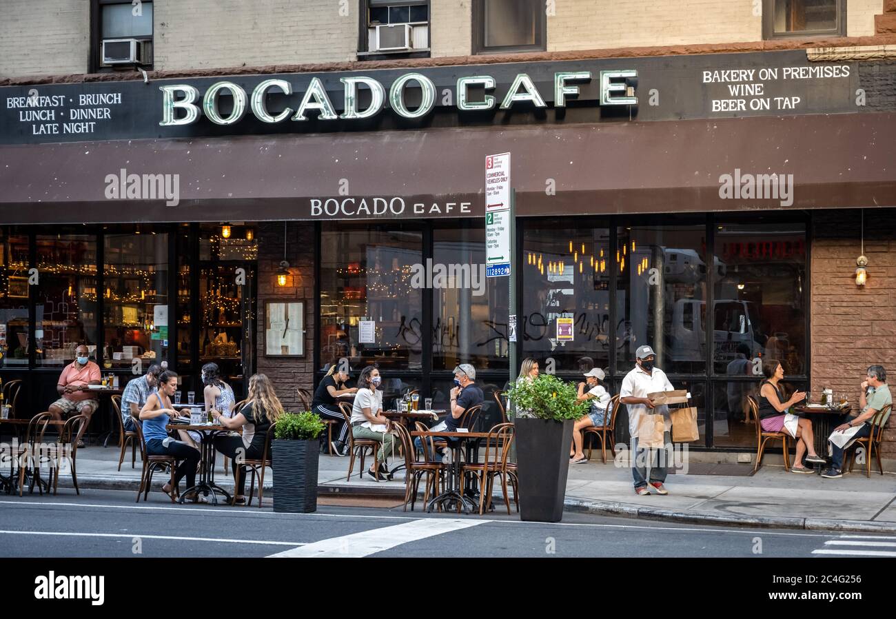New York, Stati Uniti. 26 Giugno 2020. Un addetto alle consegne si fa strada tra i tavoli allestiti all'esterno nella Lexington Avenue dell'Upper East Side, in quanto i ristoranti sono stati autorizzati ad aprire servizi all'aperto. Le persone sono ancora tenute a osservare la distanza sociale, quando la città è entrata in una nuova fase di restrizioni rilassate fissate dall'epidemia di coronavirus. Credit: Enrique Shore/Alamy Live News Foto Stock