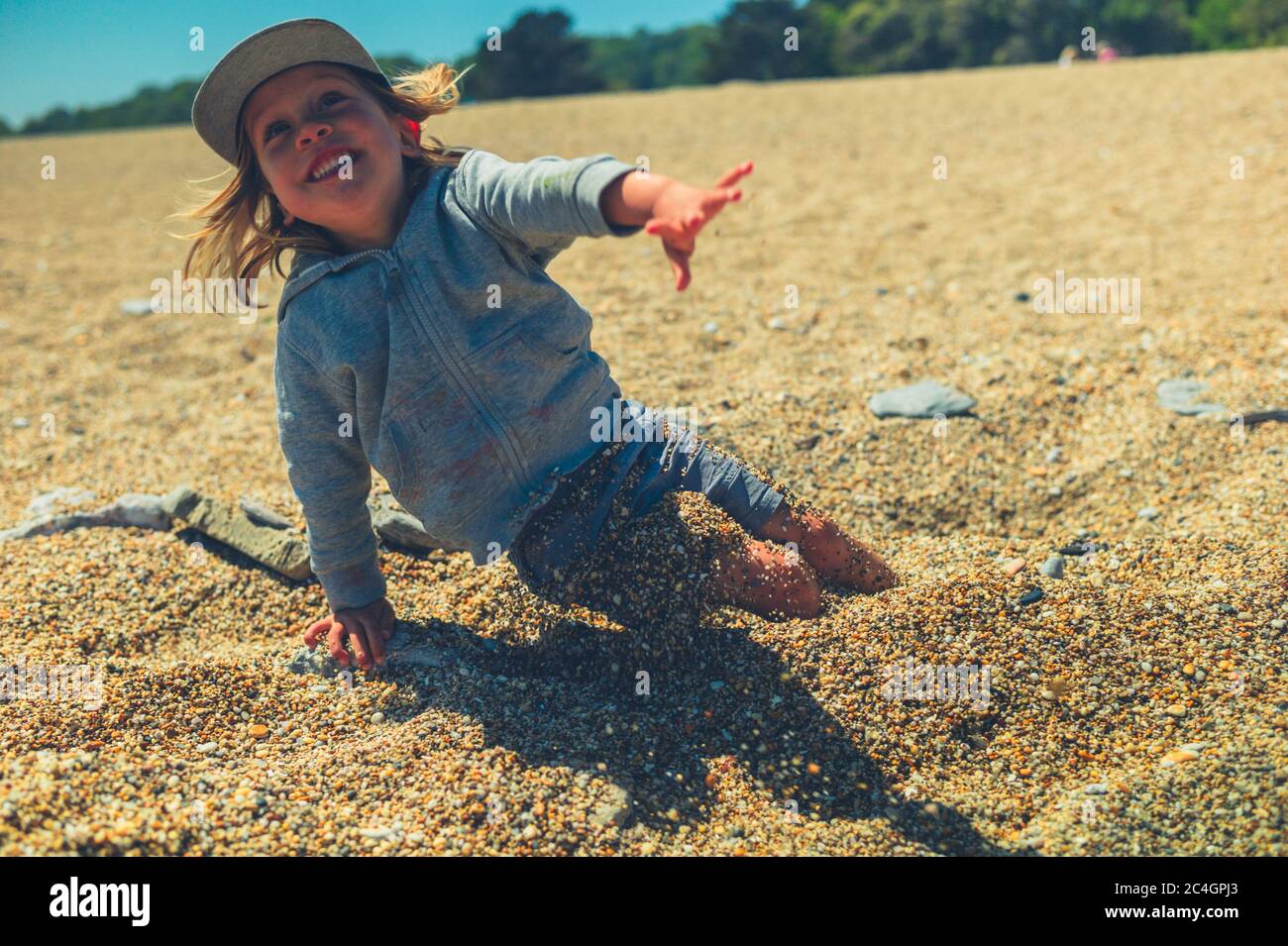 Un piccolo ragazzo preschooler sta giocando sulla spiaggia e si sta seppellendo in ciottoli Foto Stock