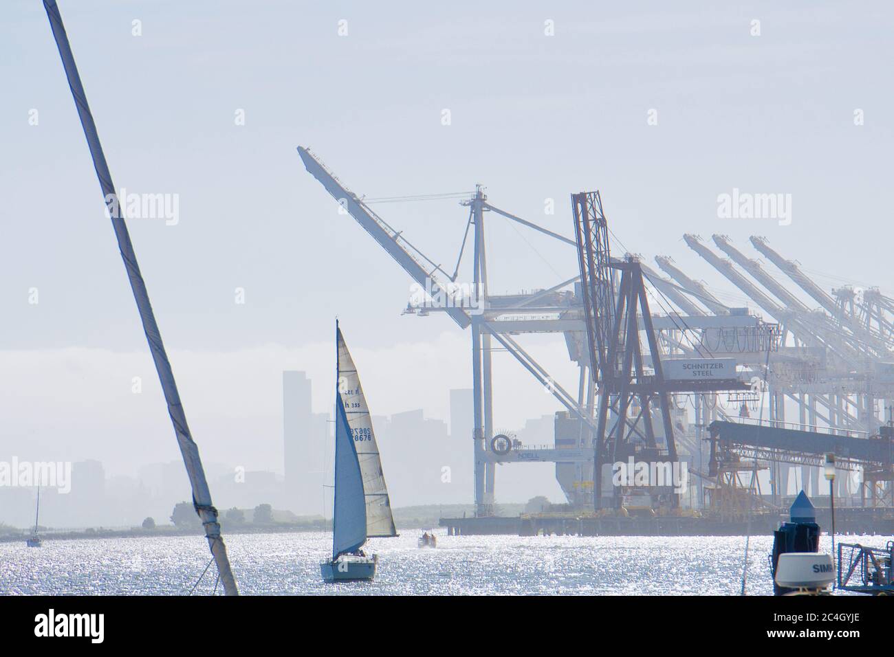 Barca a vela che entra nel porto interno di Oakland, a Jack London Square, con gru di trasporto e banchine. Bay Area turismo e ricreazione. Oakland, California, Stati Uniti. Foto Stock
