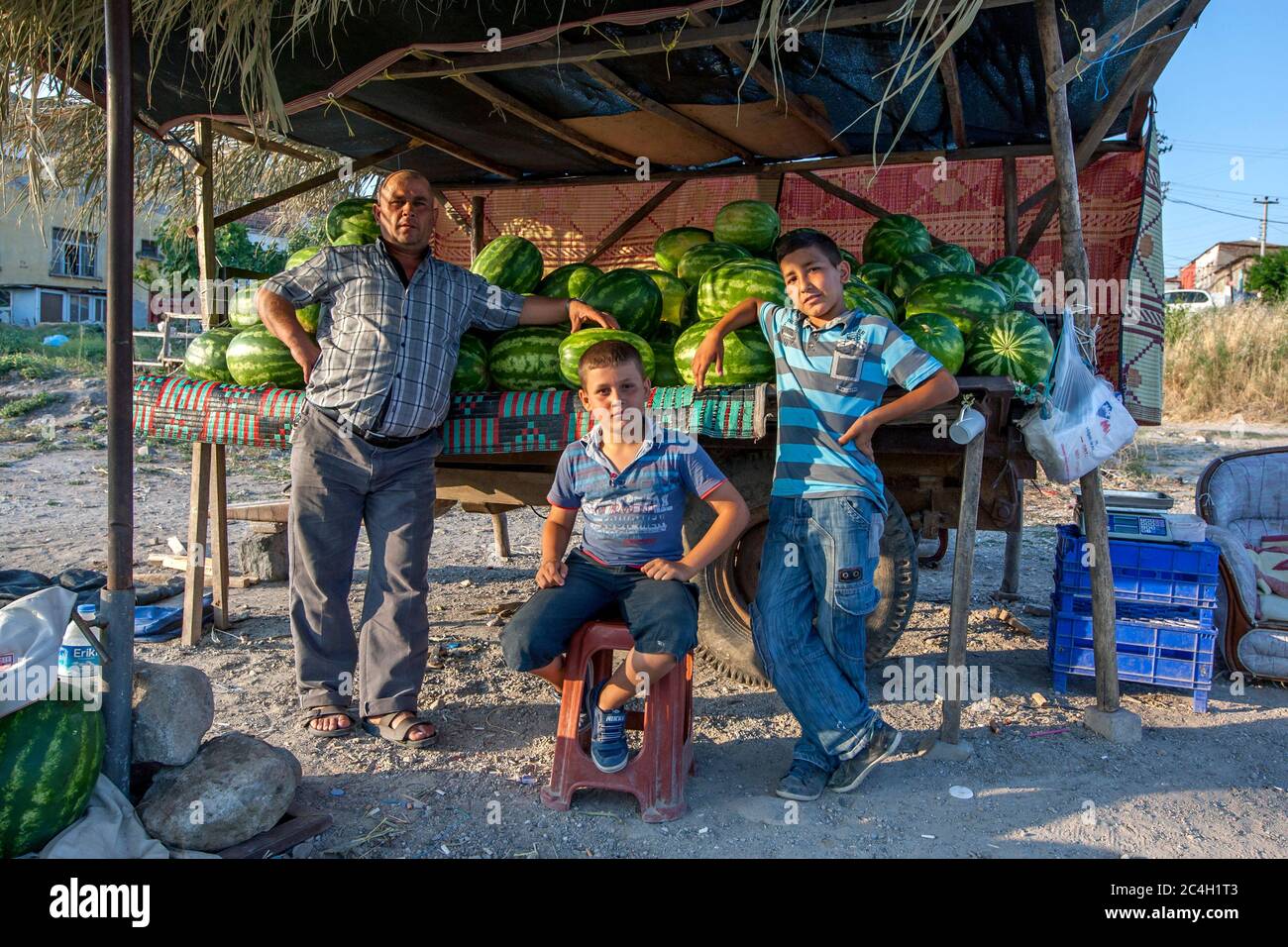 Un uomo e ragazzi turchi aspettano i clienti al loro stand angurmelone allestito su un rimorchio alla periferia di Bergama, una città nella Turchia occidentale. Foto Stock