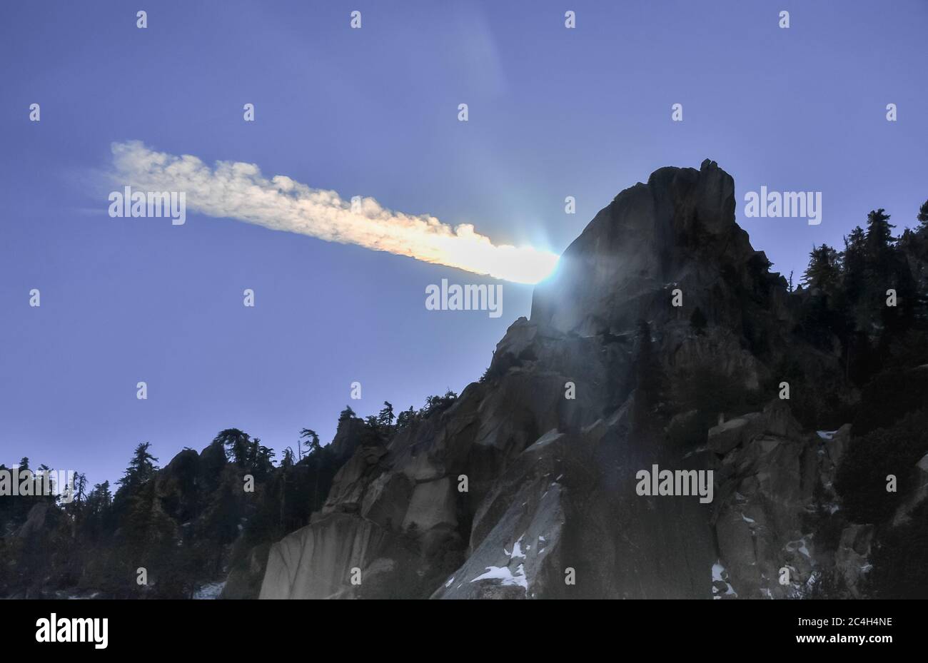 Picco di montagna scuro, che si staglia contro il cielo blu con il sole che illumina un percorso nuvoloso/a vapore. Foto Stock
