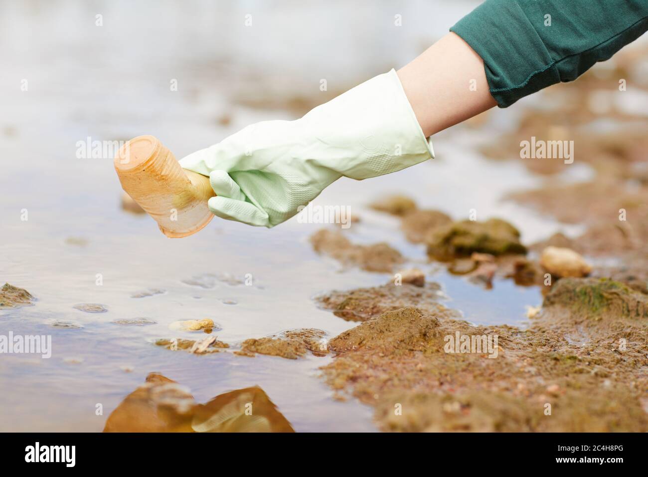 Primo piano di donna in guanti protettivi che raccolgono i rifiuti sul fiume Foto Stock