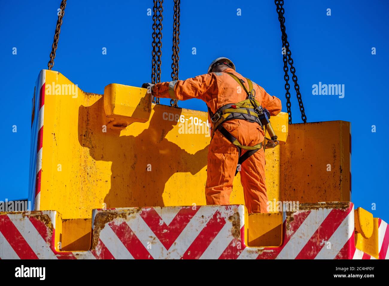 Il tecnico che indossa tute arancioni e il cappello guida il contrappeso della gru mobile in posizione Foto Stock