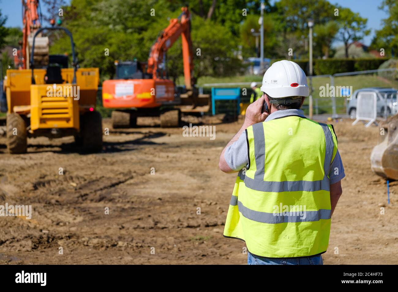 Lavoratore di costruzione in gilet hi-vis e elmetto fa la chiamata del telefono mobile sul luogo della costruzione Foto Stock