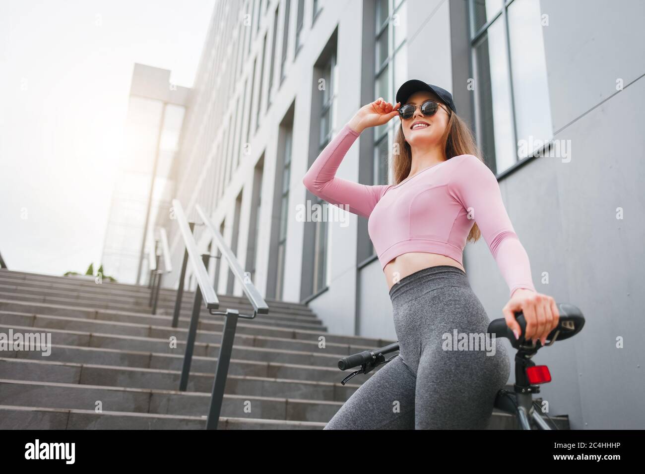 Ragazza snella in abbigliamento sportivo si trova vicino alla costruzione di un centro business appoggiato su una bicicletta Foto Stock