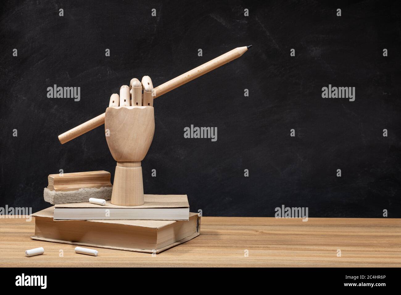 Mano di legno che tiene una matita sui libri. Sfondo lavagna. Concetto di ritorno a scuola. Spazio di copia Foto Stock