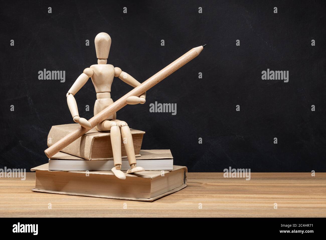 Manichino di legno che tiene una matita seduta su un mucchio di libri. Ritorno a scuola Foto Stock