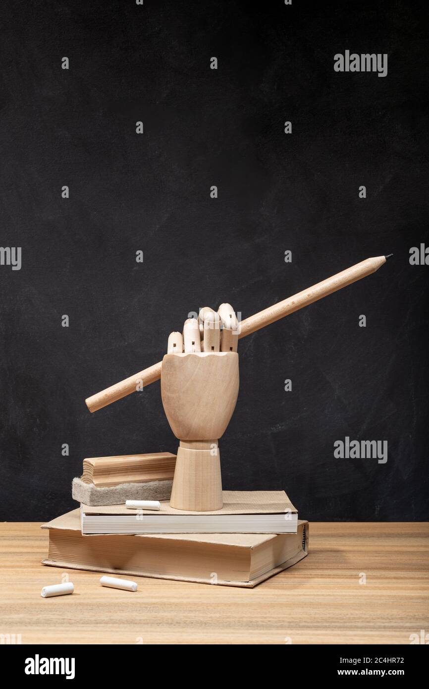 Mano di legno che tiene una matita sui libri. Sfondo lavagna. Concetto di ritorno a scuola. Spazio di copia Foto Stock