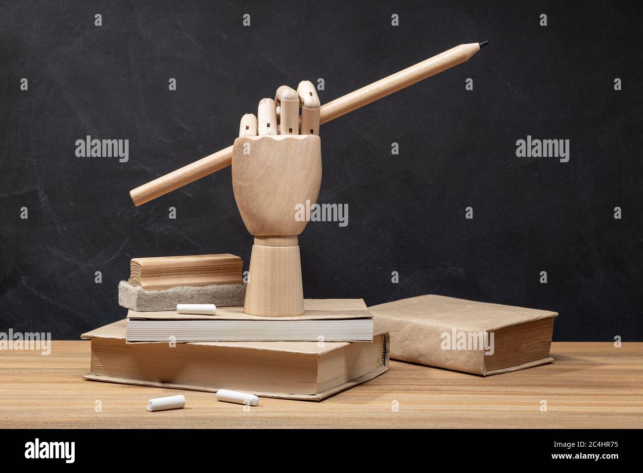 Mano di legno che tiene una matita sui libri. Sfondo lavagna. Concetto di ritorno a scuola. Spazio di copia Foto Stock
