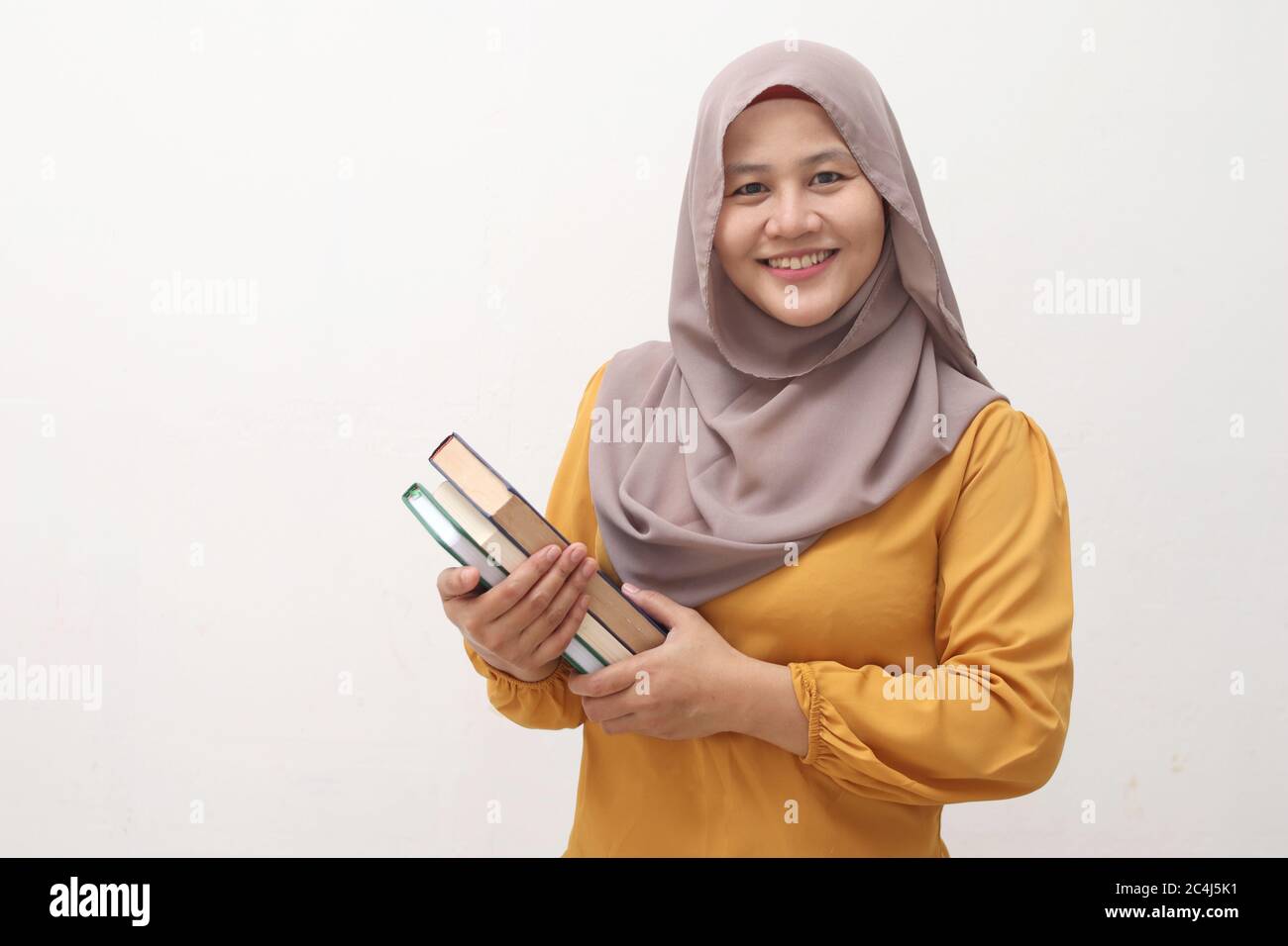 Ritratto di giovane donna musulmana d'affari che indossa hijab tenendo libro e sorridente, educativo o attività di svago concetto, isolato su bianco Foto Stock